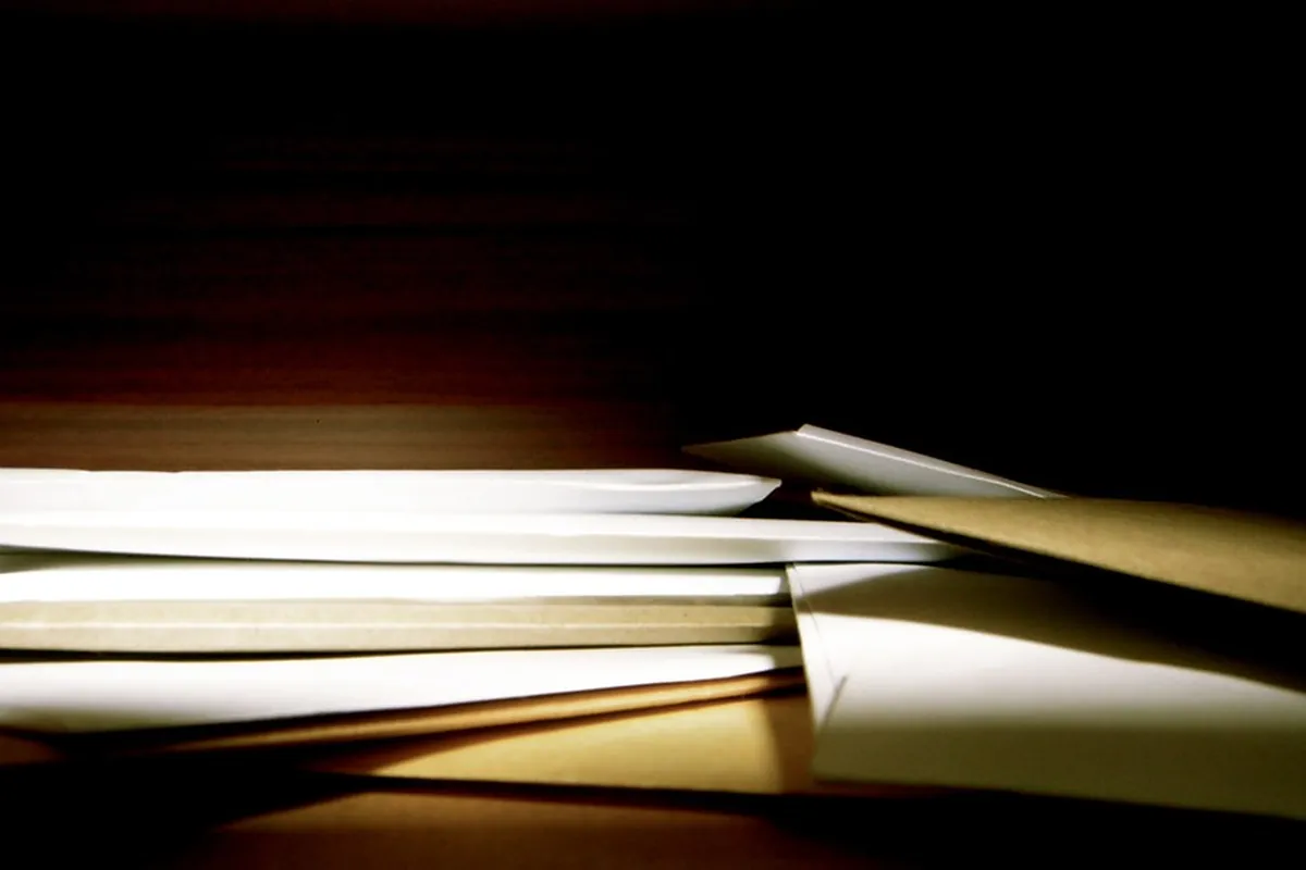 A stack of white and brown envelopes on a table, lit from the side